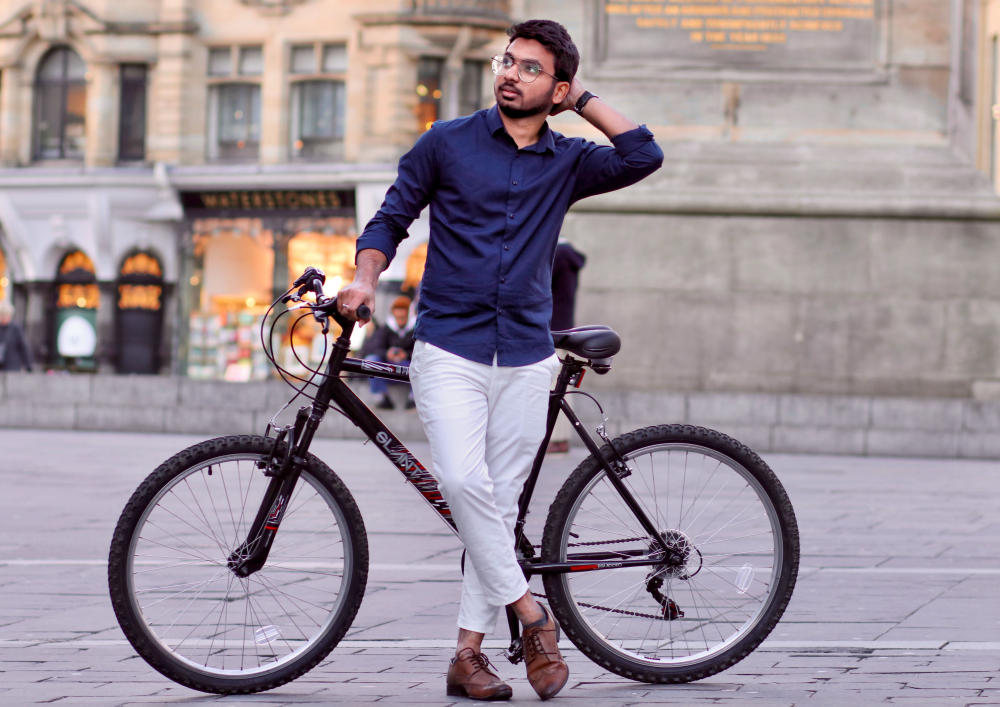 Guy in a navy shirt posing with his bicycle in a city square