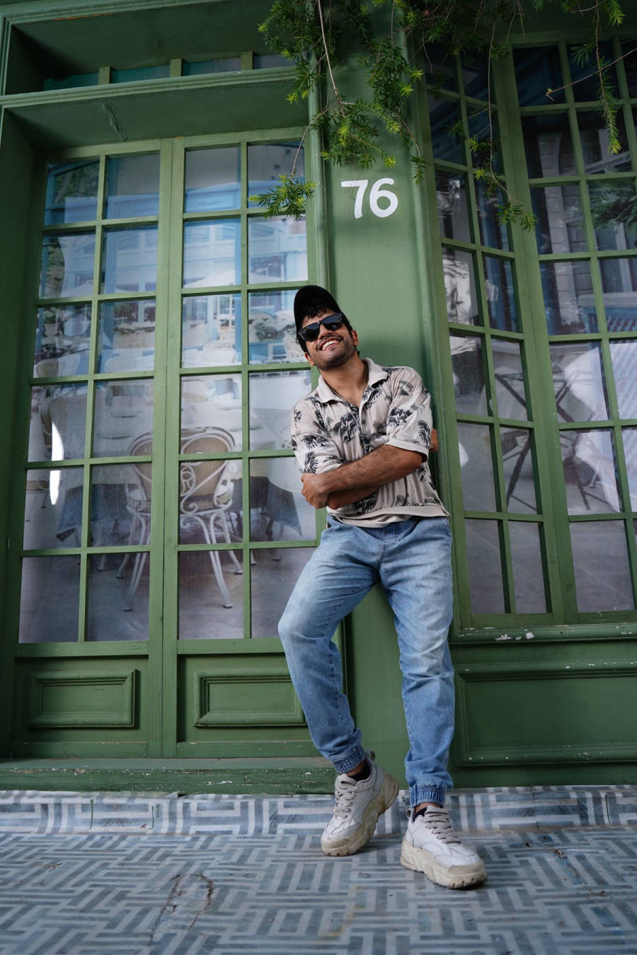 Smiling guy in printed shirt and baggy jeans against green doors
