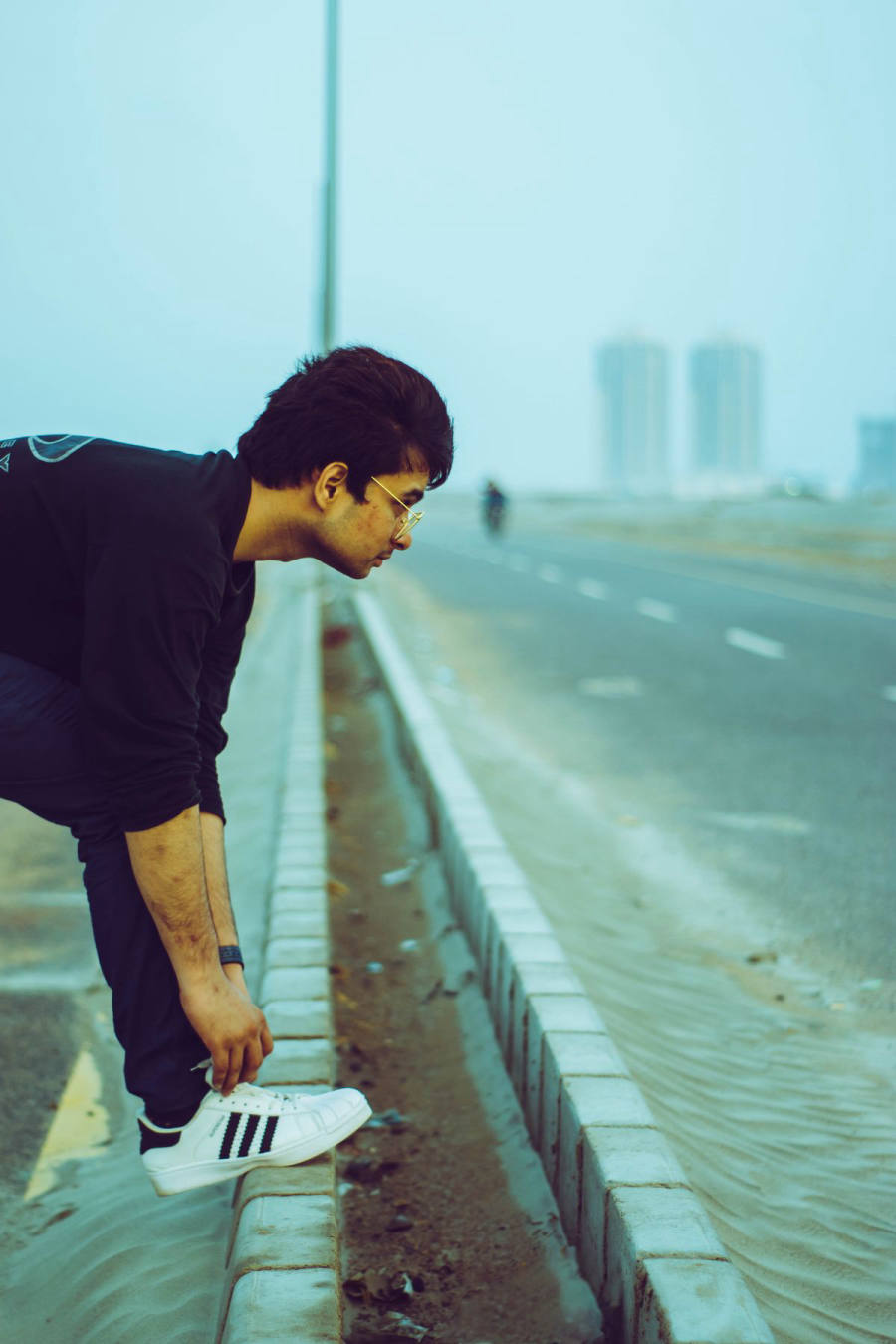 Guy tying white sneakers on a Karachi road